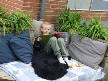 Dreng sidder og læser udenfor med puder og tæpper omkring sig
